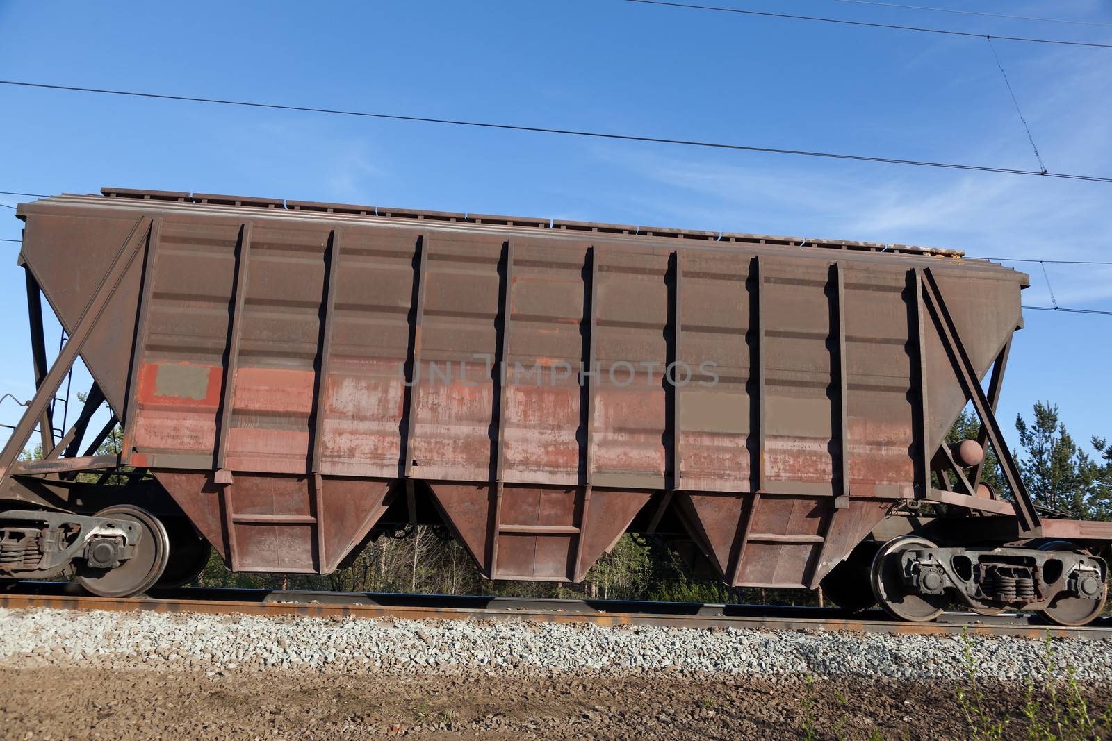 The rail car of a freight train. In a forest and blue sky.