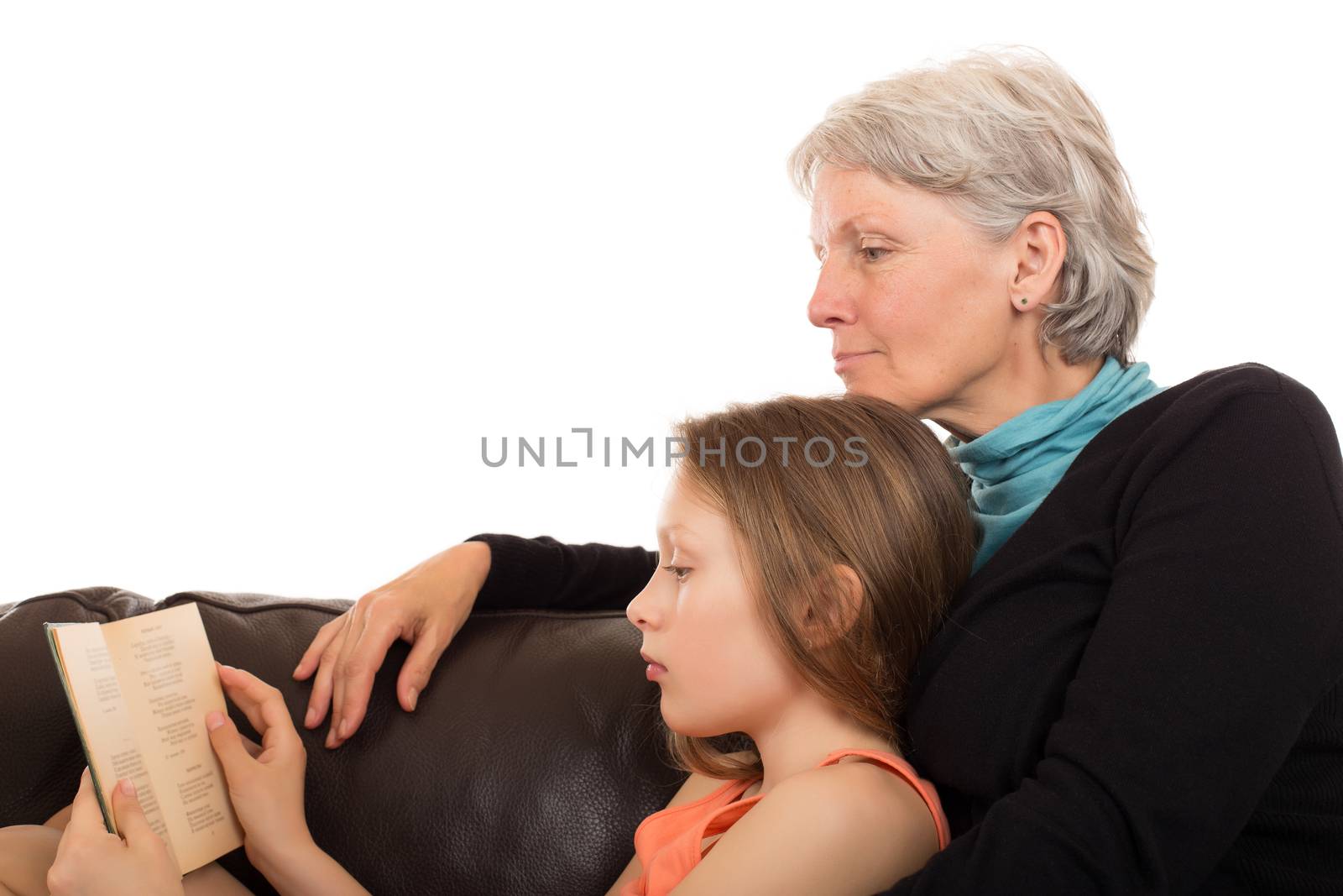 Grandmother and her granddaughter read with serenity a great story in a brown leather sofa. Isolated on white background.
