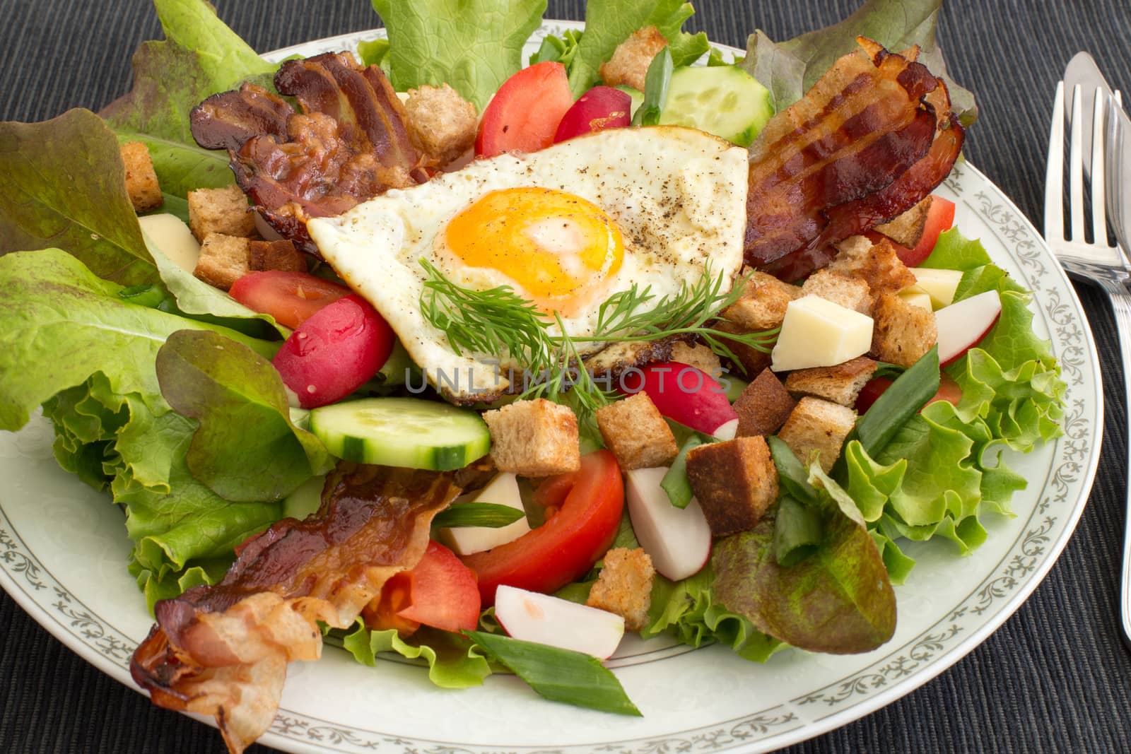 Country salad also called peasant salad, greek salad or village salad. Composed with lettuce, cucumber, onion, radish, fried egg and bacon, cheese, tomatoes, parsley and croutons.