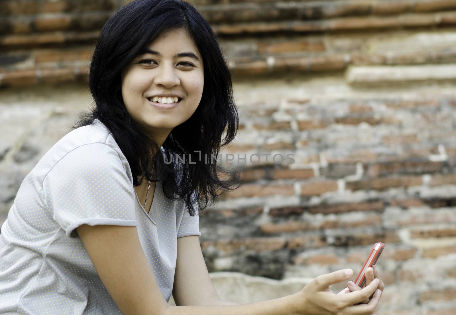 Smiling woman holds her phone with brick background