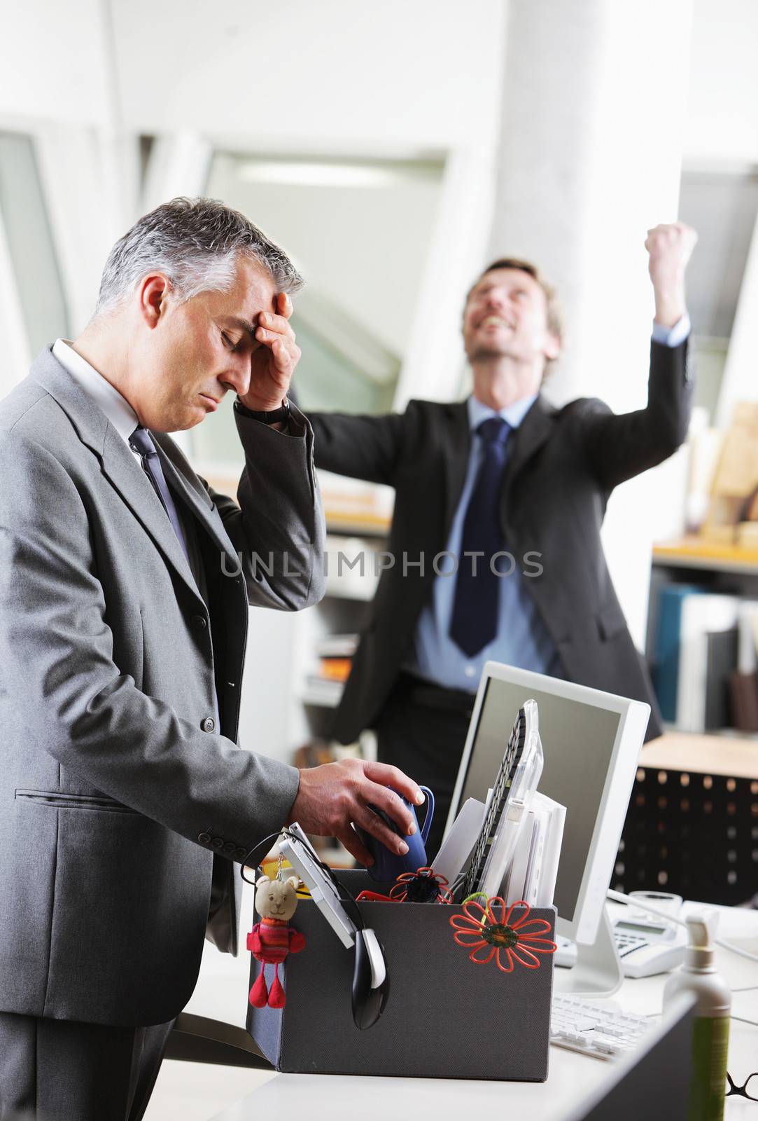 Dejected fired office worker. His colleague is celebrating on the background