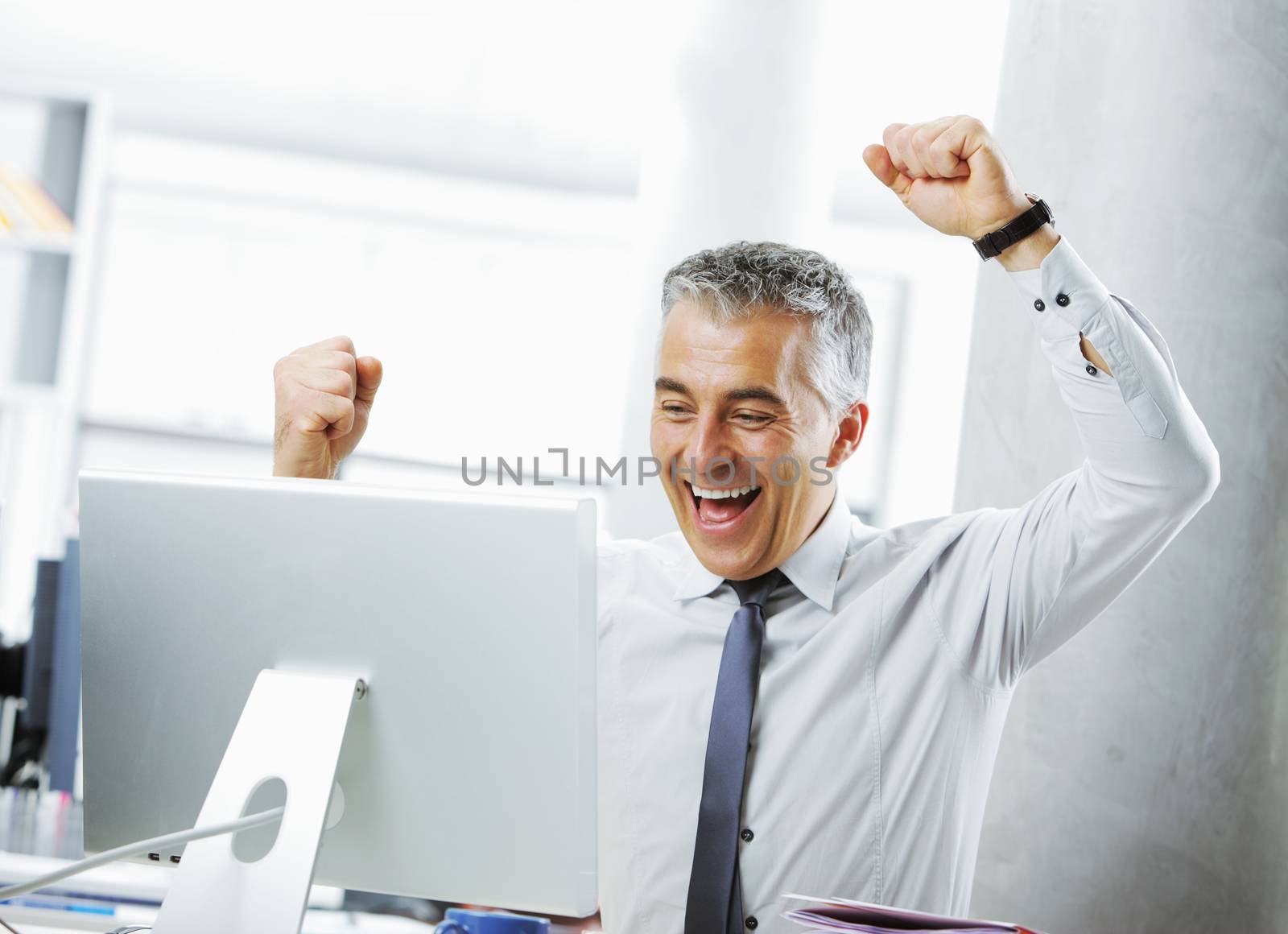 Happy mature businessman in office arms raised. 
