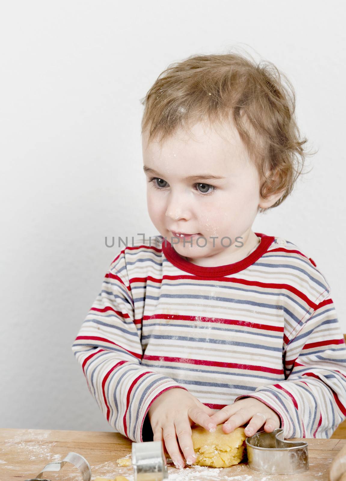 vertical image of 2 year old child making biscuit  at wooden desk