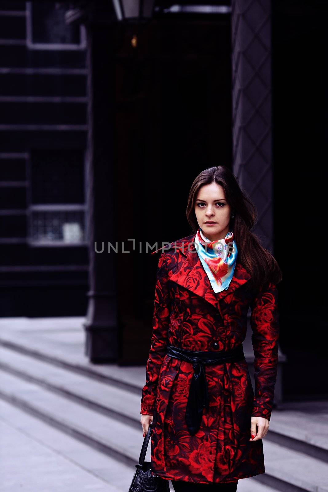 Beautiful business woman in a red cloak against expensive office building