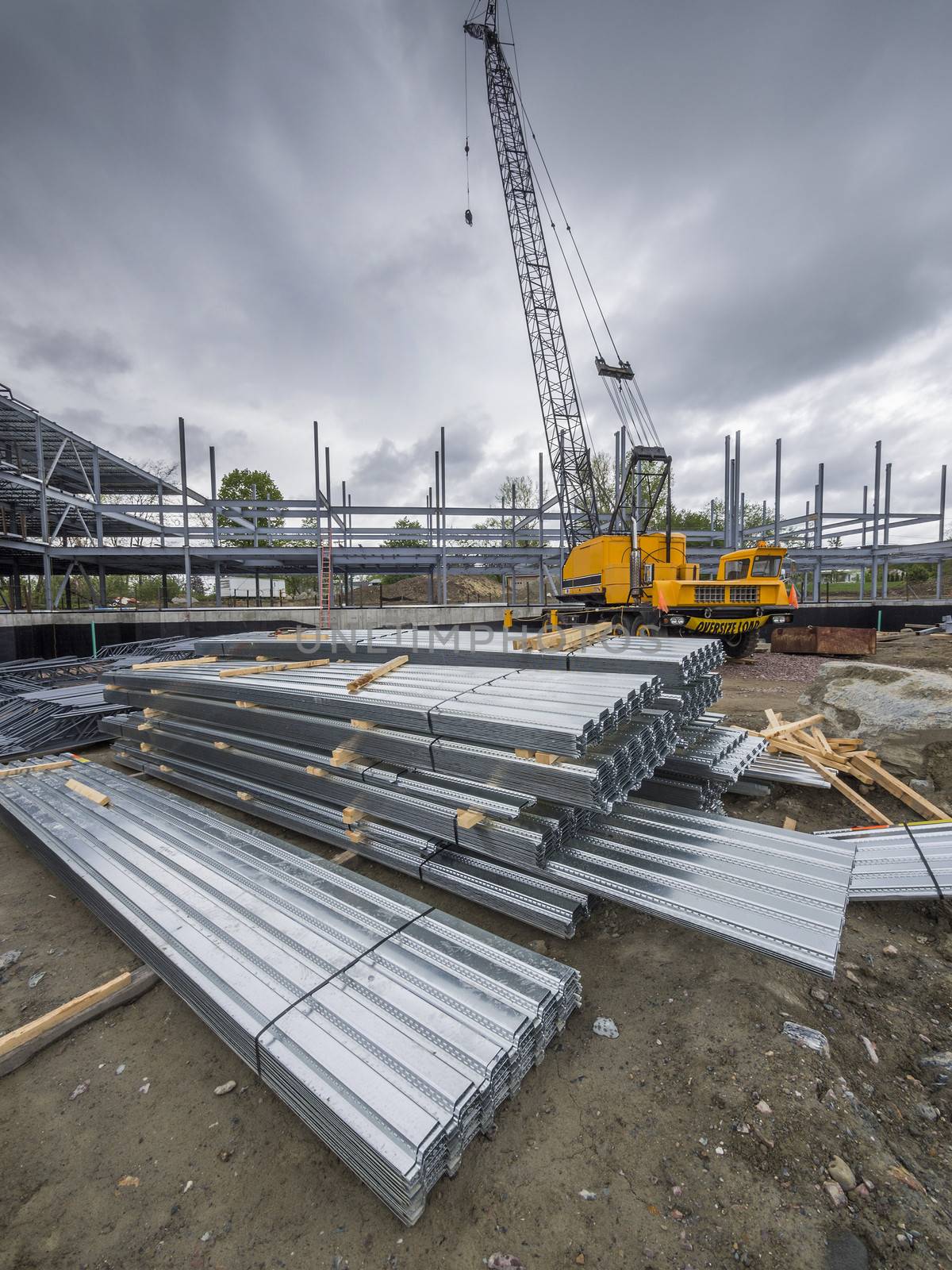 Construction site with crane and building with steel roofing material in foreground