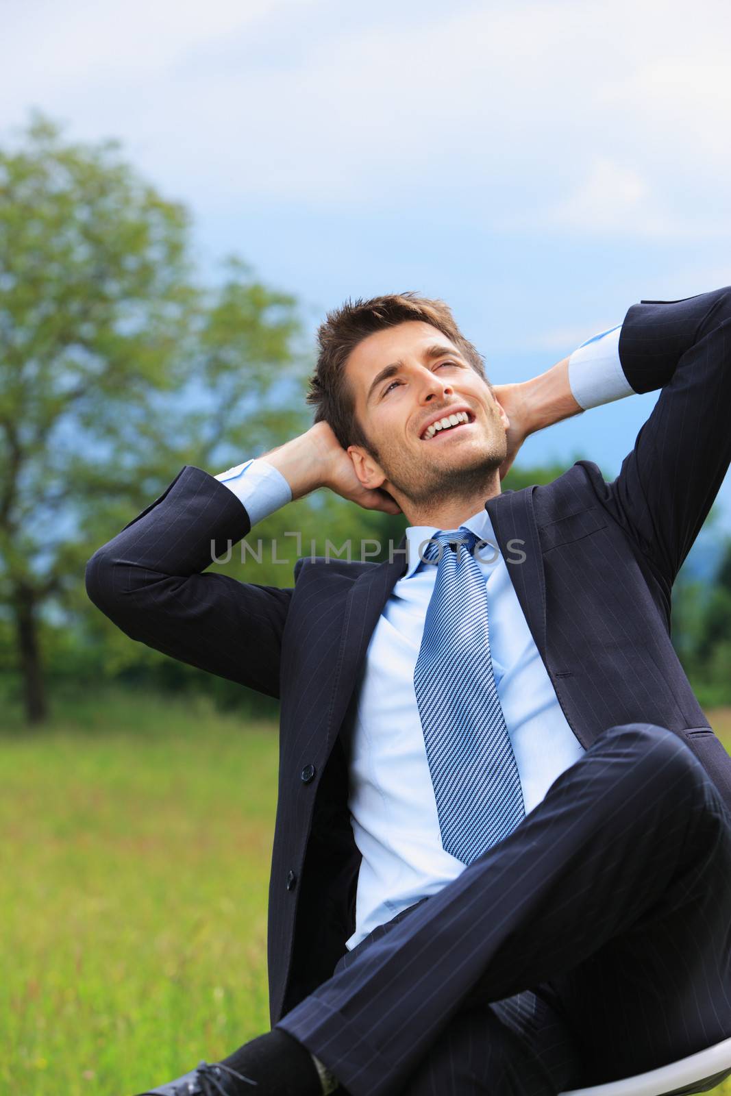 Businessman is sitting on chair in a green meadow