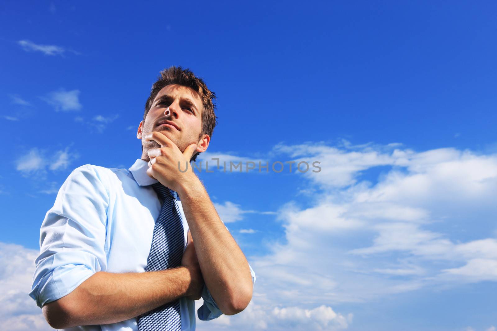 Young business man thinking against blue sky