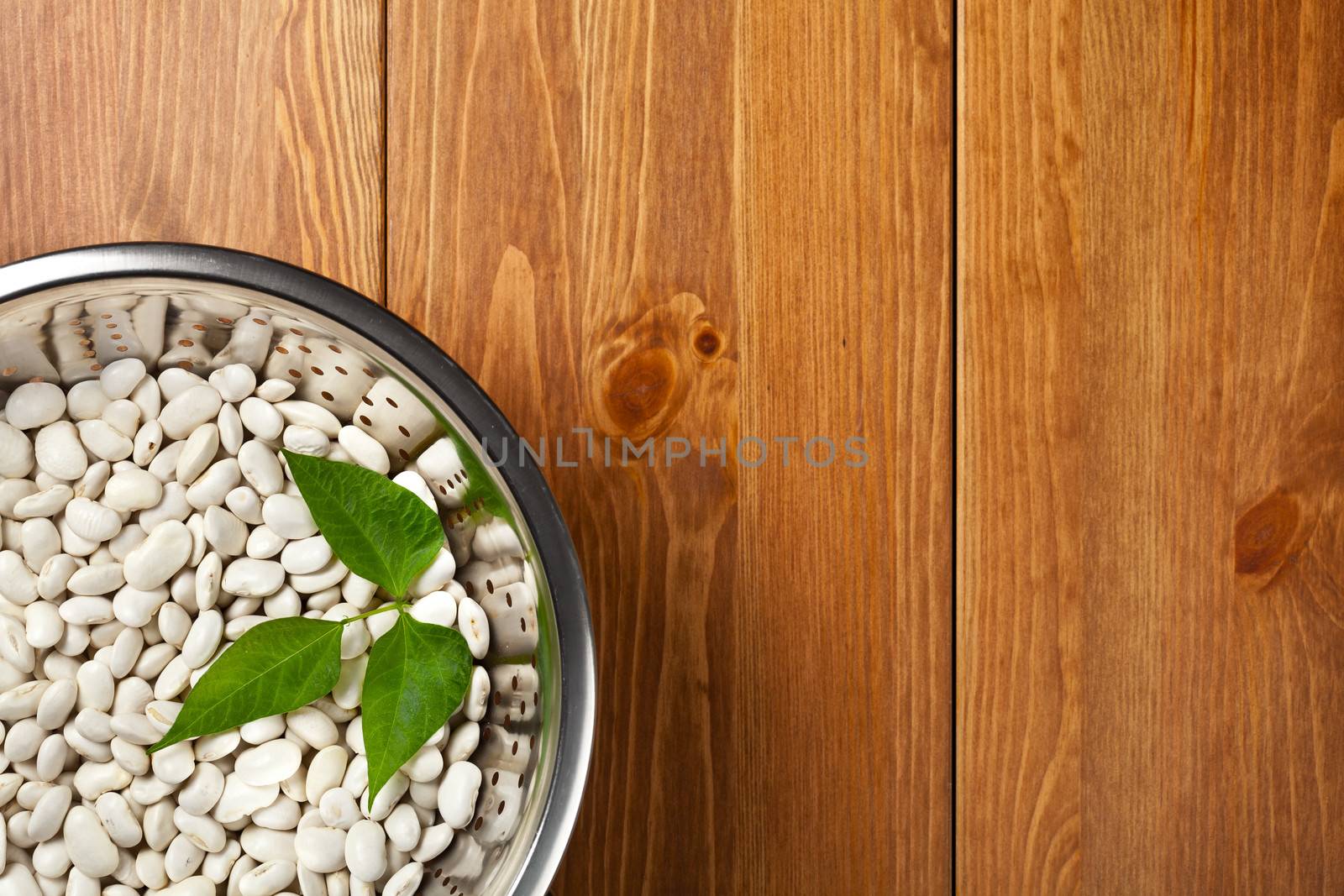 White beans in colander on wooden table background. Top view