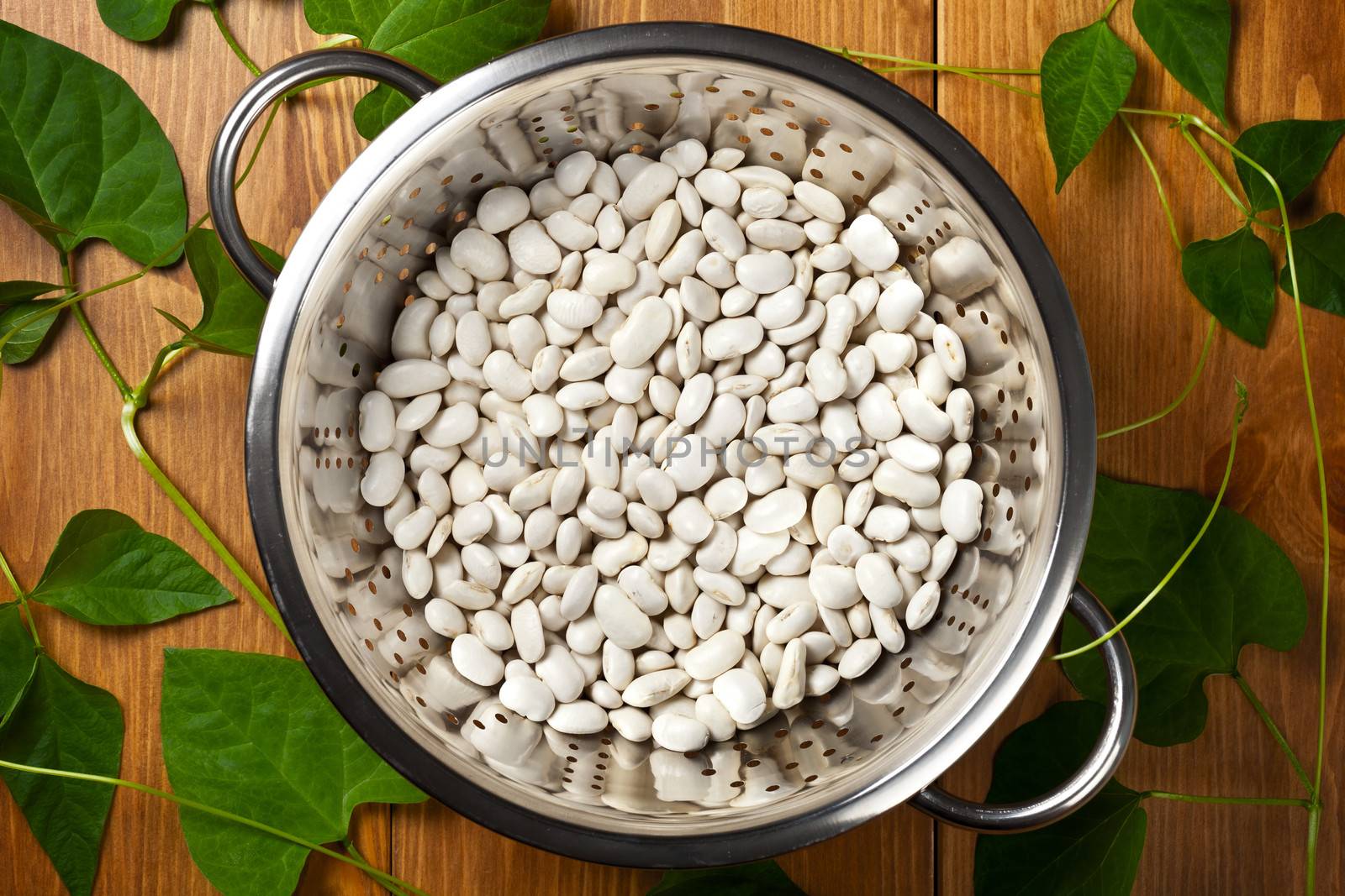White beans with green leaves on wooden table background. Top view