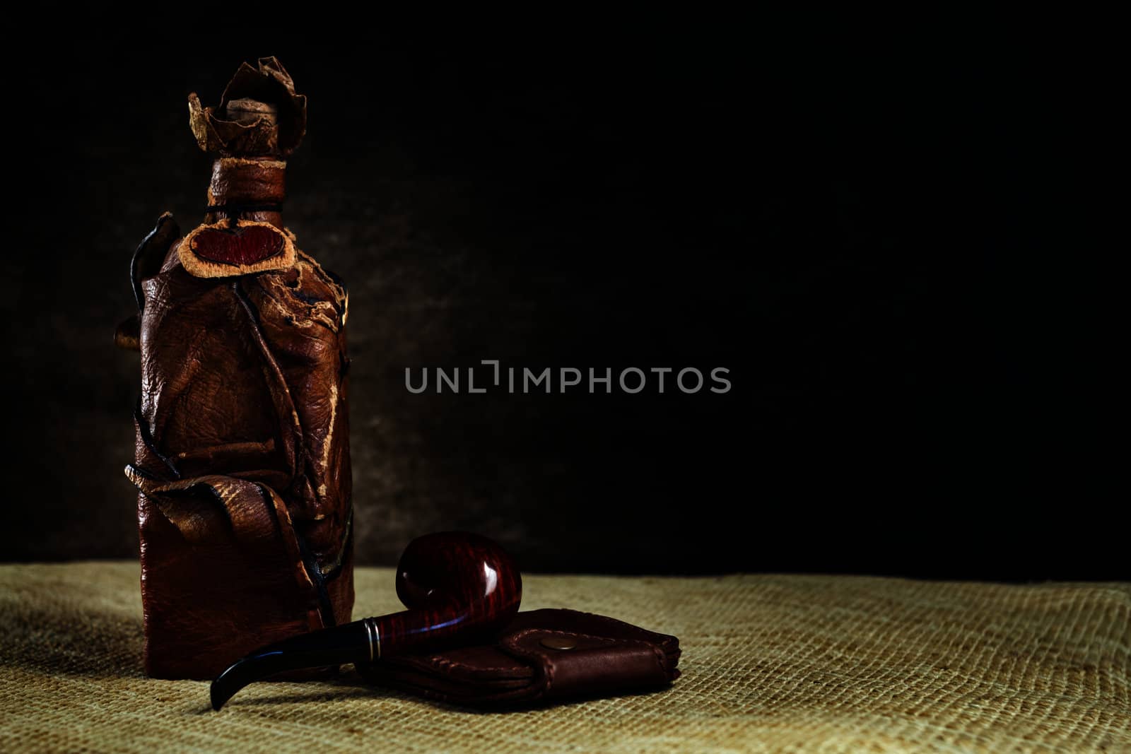 Brown leather vintage bottle with a pipe and a purse on a dark background