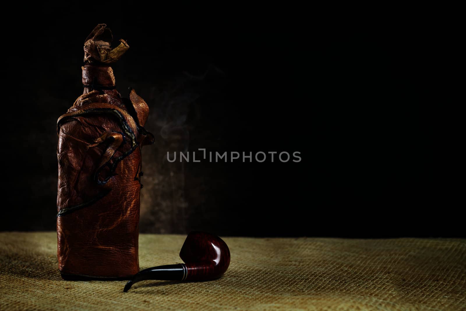 Leather vintage bottle with a pipe on a dark background by dedron
