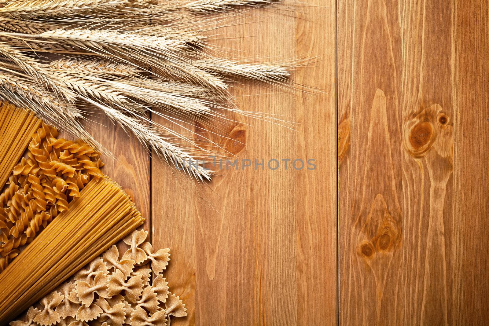 Pasta with wheat ear on wooden background. Different types of whole wheat pasta. Top view. Copy space