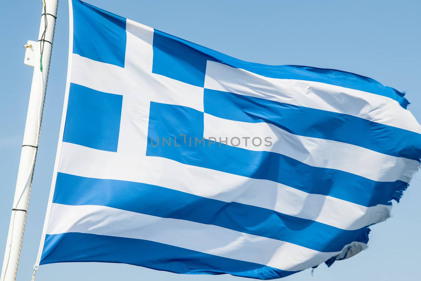 Greek flag waving in the wind against a blue sky