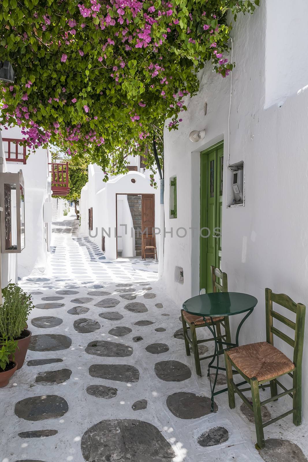 Narrow street in Mykonos with flowers, table and chairs