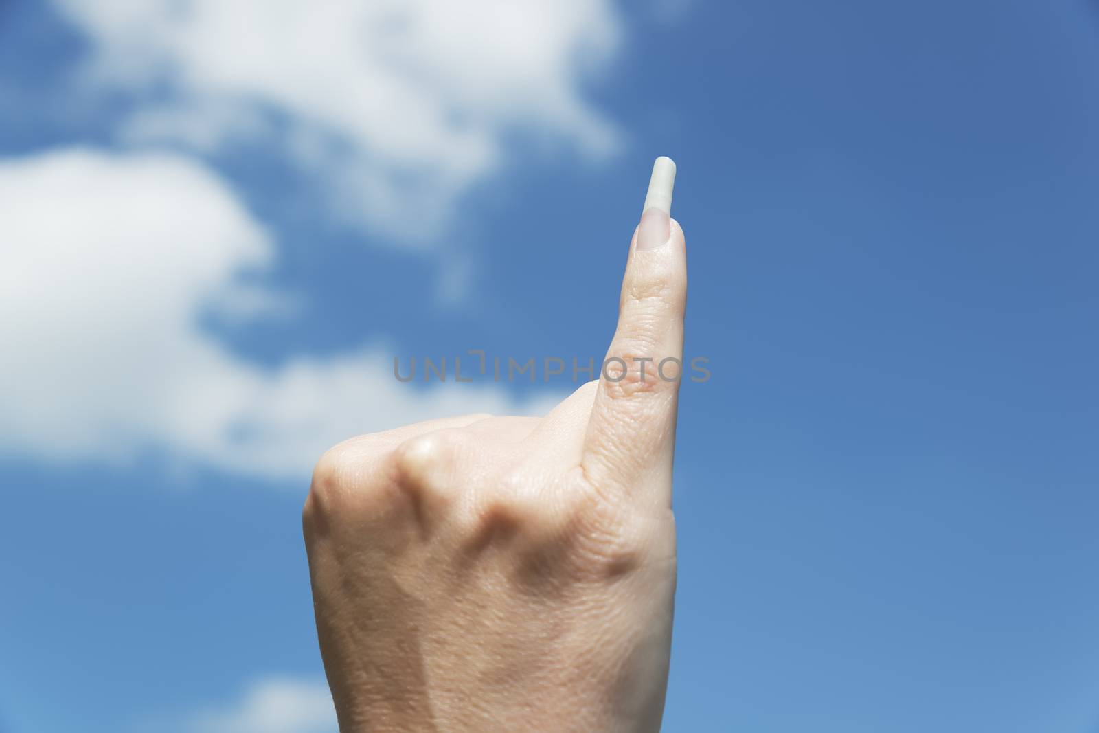 Hand of woman with long fingernail against blue sky and white clouds