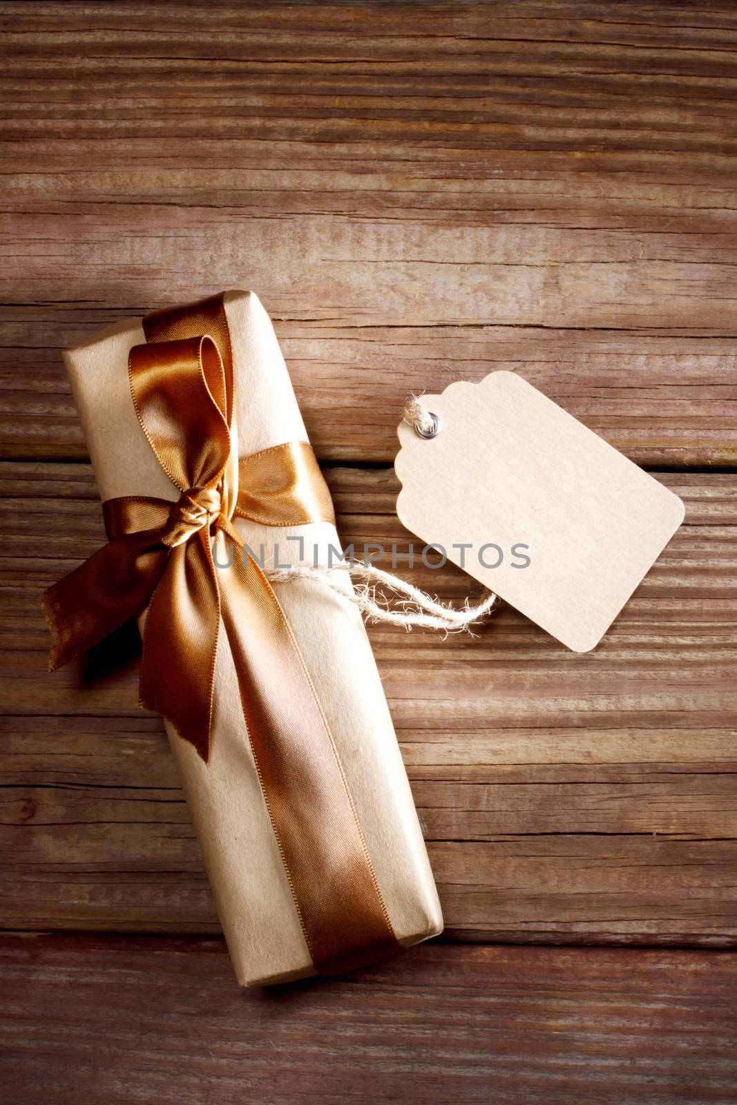 Brown rectangular present box on a rustic wood table with a bow and a blank label