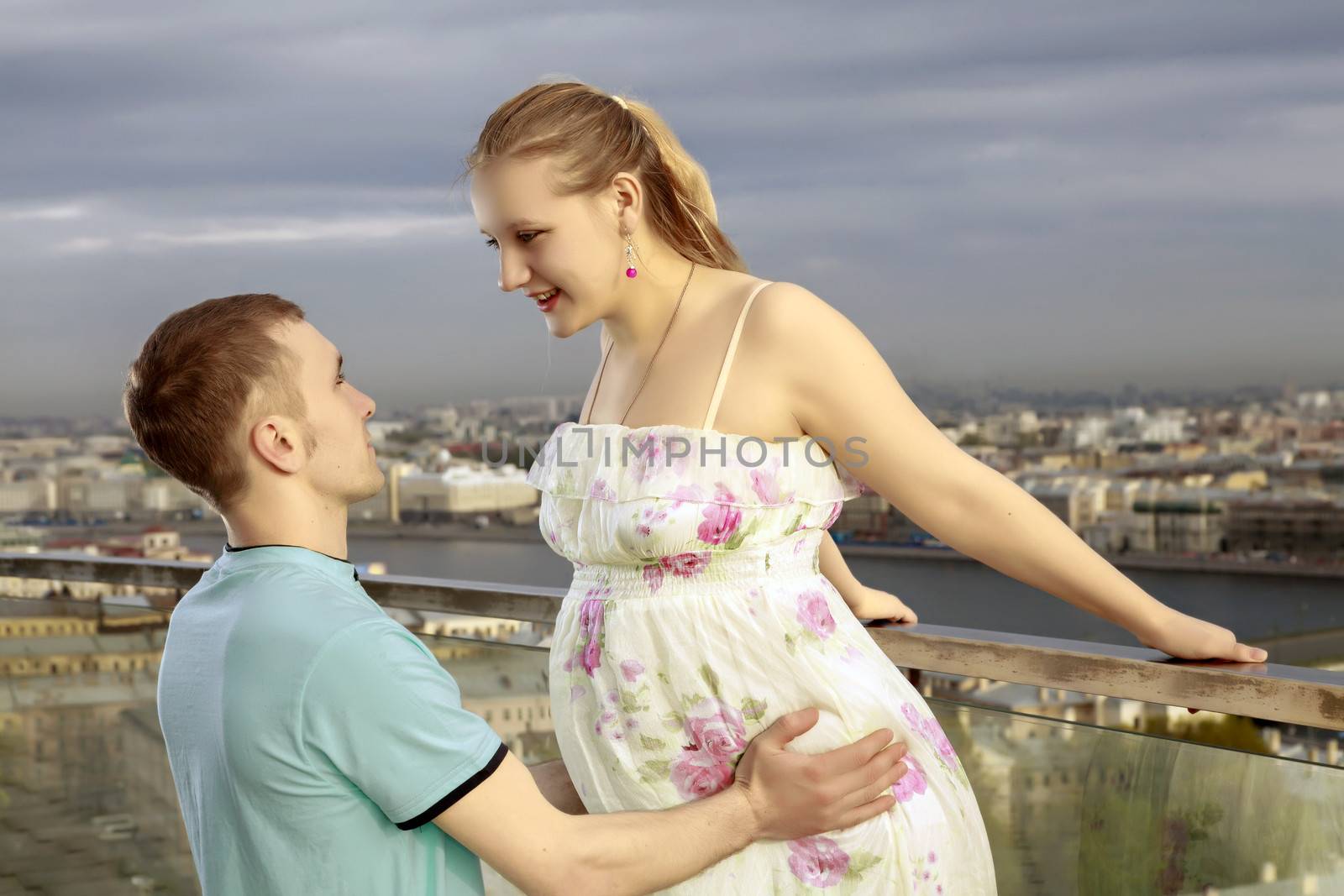 A young couple expecting a baby. Happy couple walking on the roof of a high building, with views of the big city.