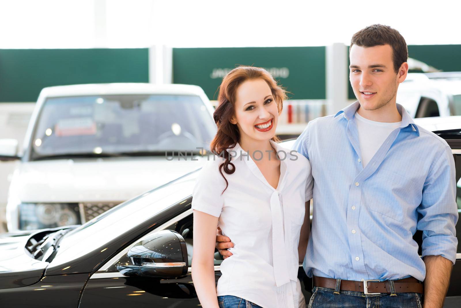 Young couple standing embracing near a car in the showroom