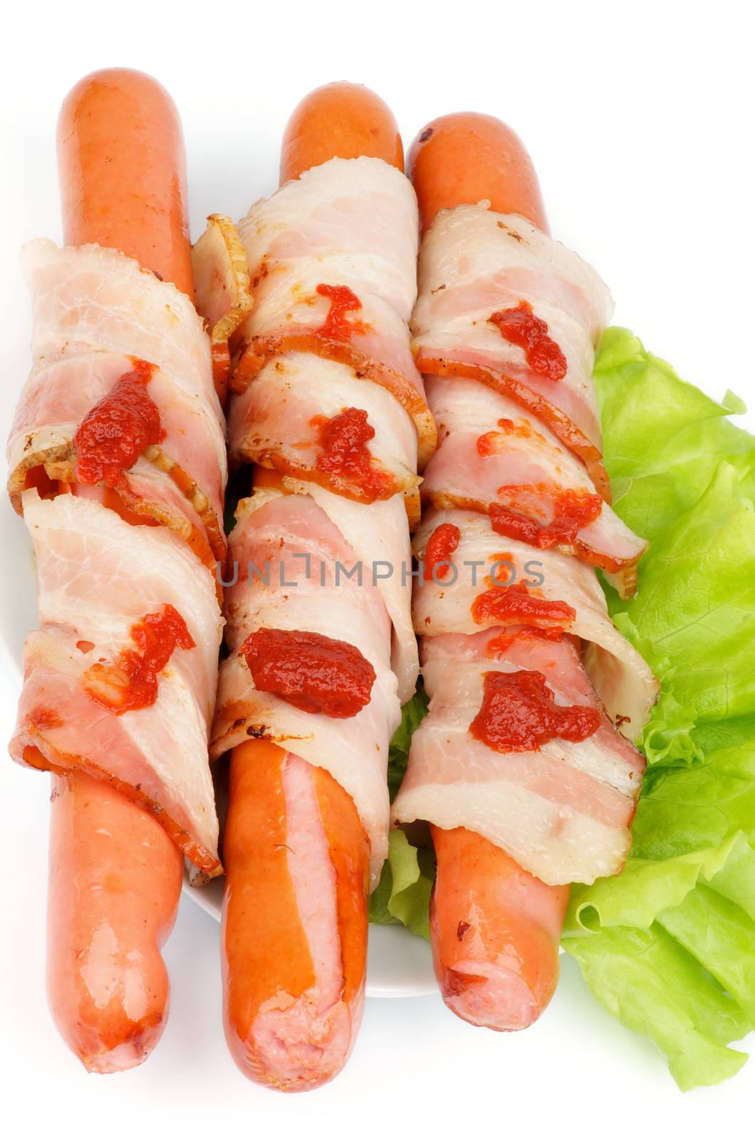Three Pork Sausages Wrapped in Bacon Garnished with Lettuce and Ketchup isolated on white background