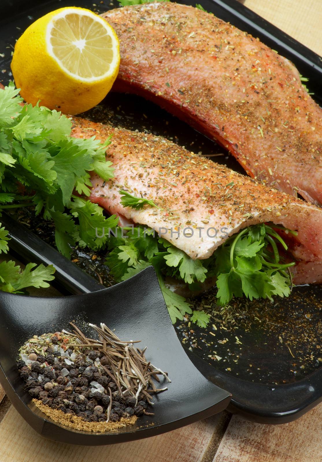 Preparing to Frying Red Snapper Fish with Parsley, Bowl of Spices and Lemon on Black Baking Tray on Wooden background