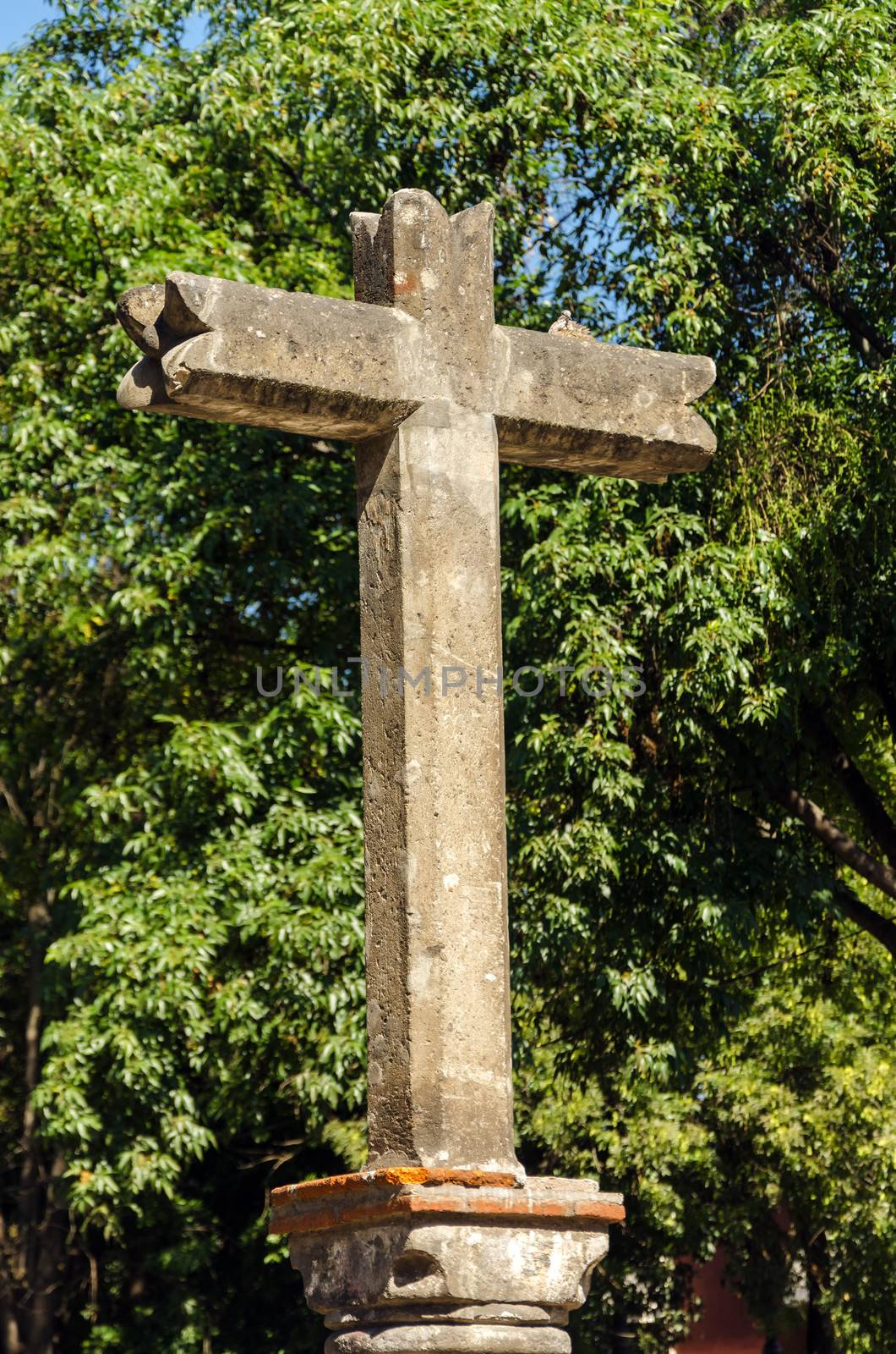 A stone cross in Mexico City with lush green trees in the background