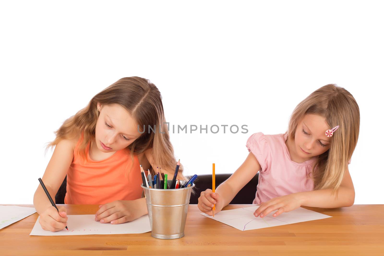 Two concentrated children draw on a wooden table. Isolated on a white background.