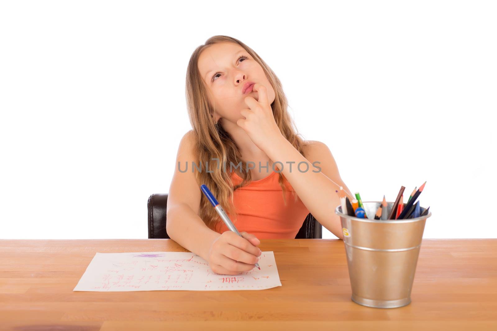 Child sitting at a wooden table trying to make a drawing. Isolated on a white background.