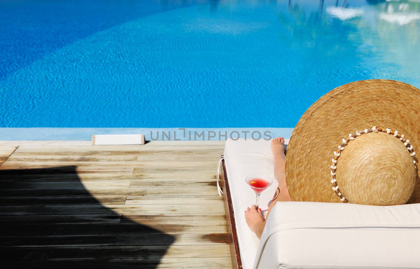 Woman in hat relaxing at the poolside with cosmopolitan cocktail