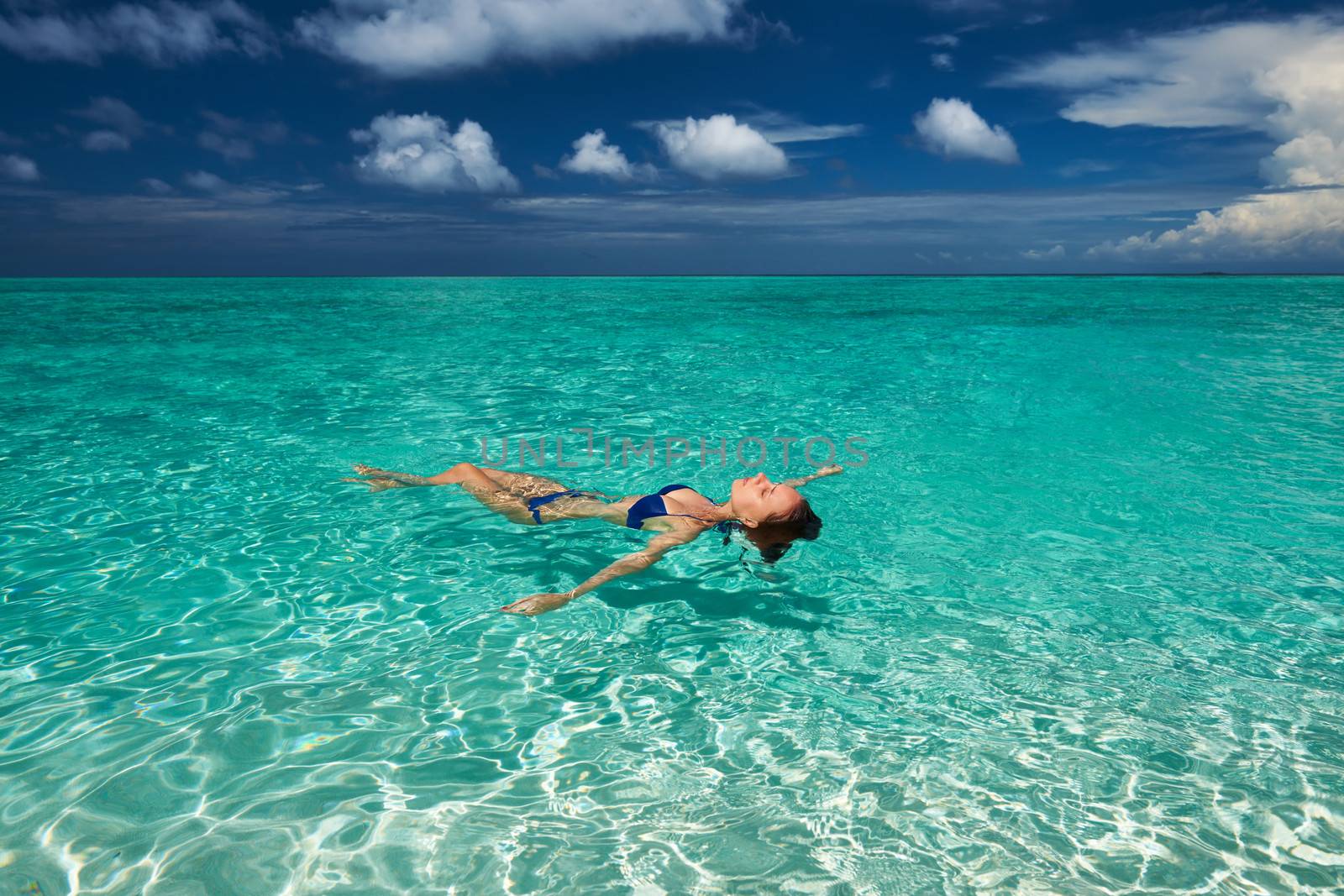 Woman in bikini lying on water at tropical beach