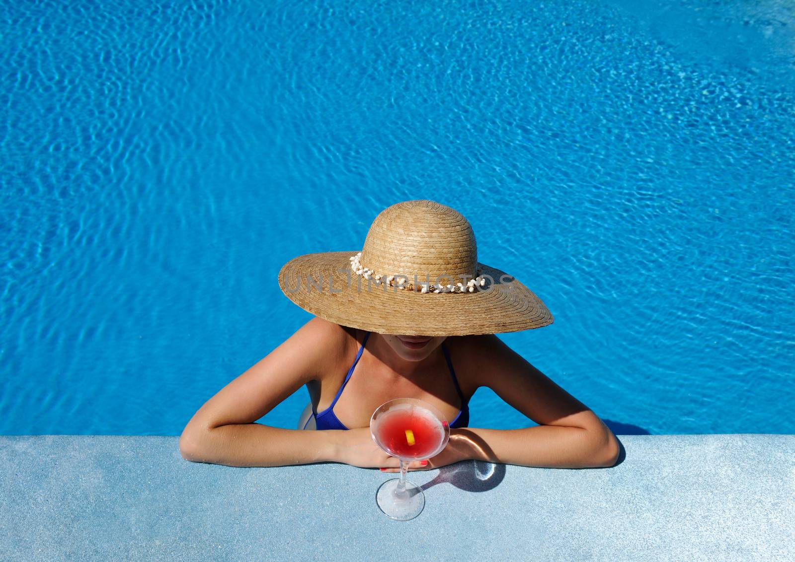 Woman in hat relaxing at the pool with cosmopolitan cocktail