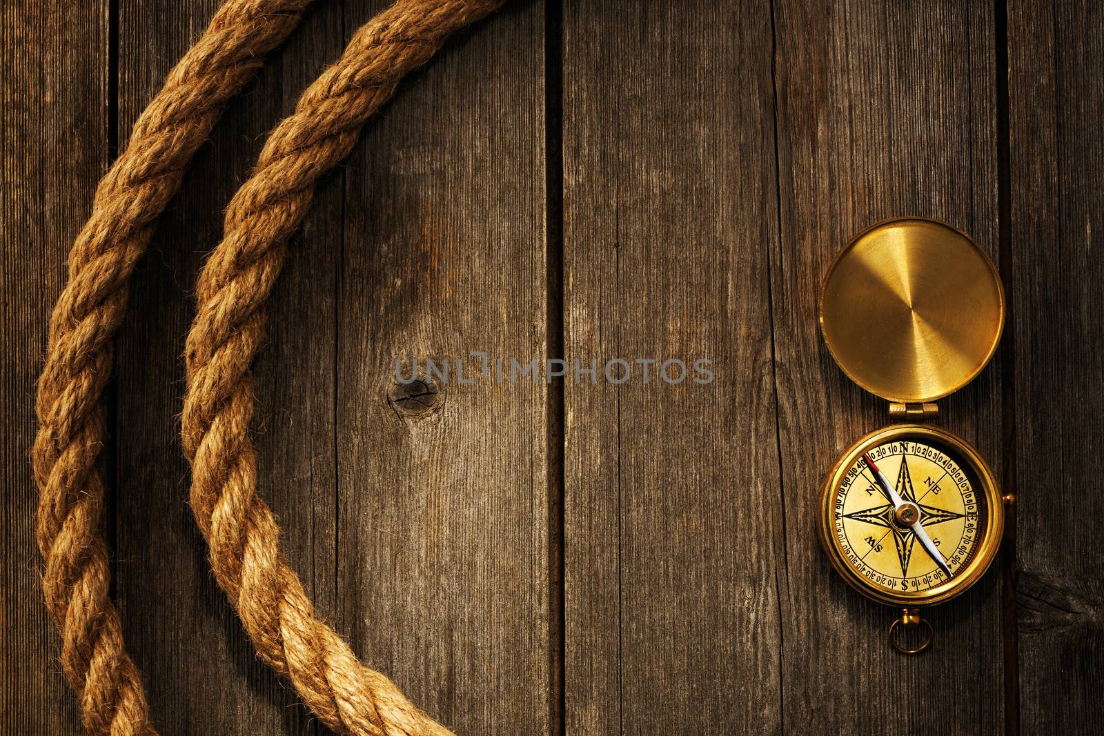 Antique brass compass and rope over wooden background
