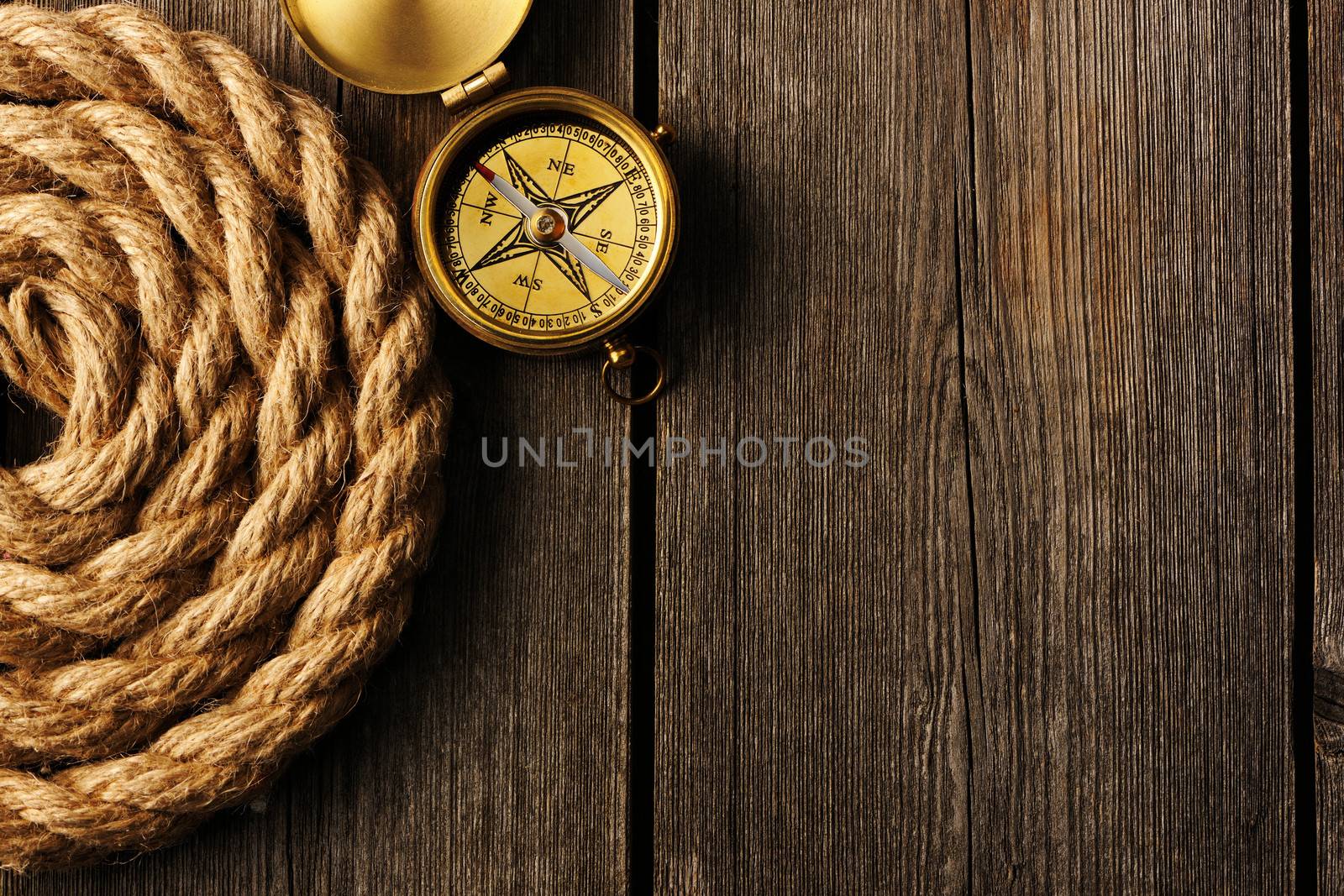 Antique brass compass and rope over wooden background