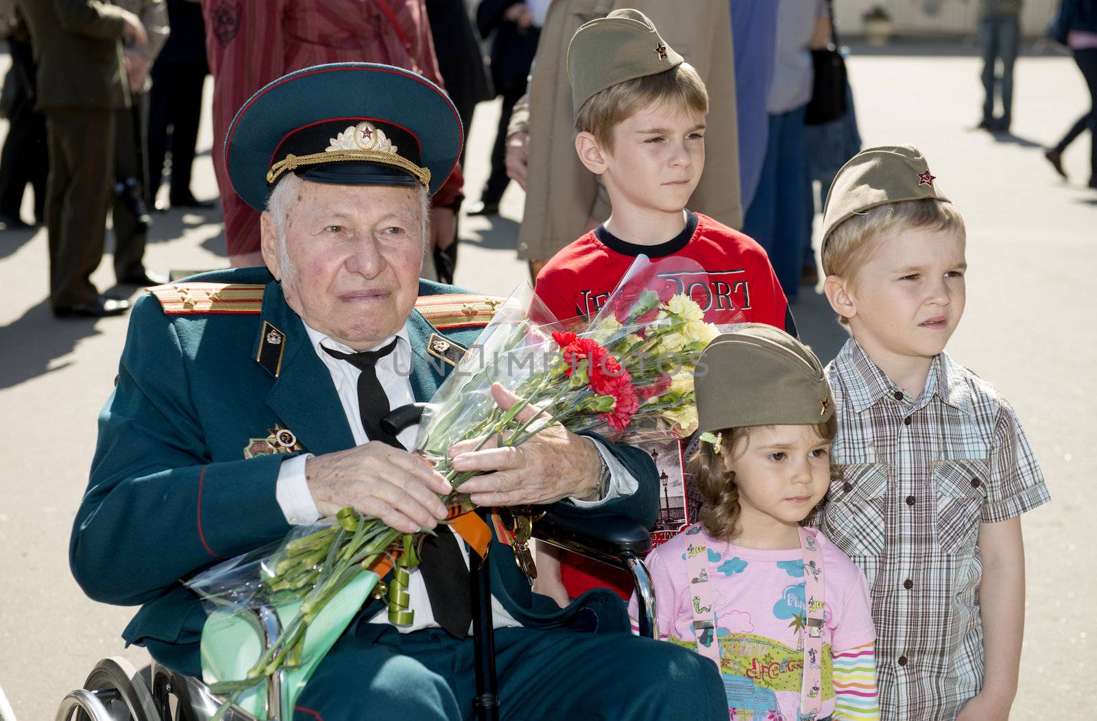 Moscow, Russia - May 9, 2013: Old man veteran of WWII in uniform decorated with numerous orders and medals bearing bunch of flowers and three children during festivities devoted to 68th anniversary of Victory Day.