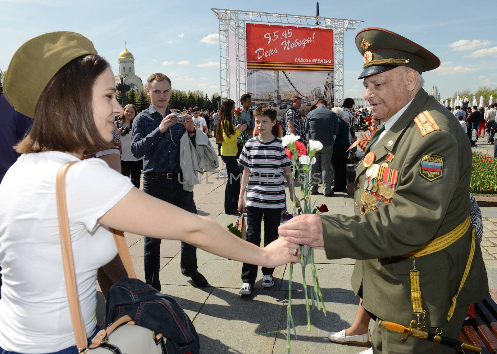  Moscow, Russia - May 9, 2013: Old man veteran of WWII in uniform decorated with numerous orders and medals bearing bunch of flowers and accept congratulations from a young girl during festivities devoted to 68th anniversary of Victory Day