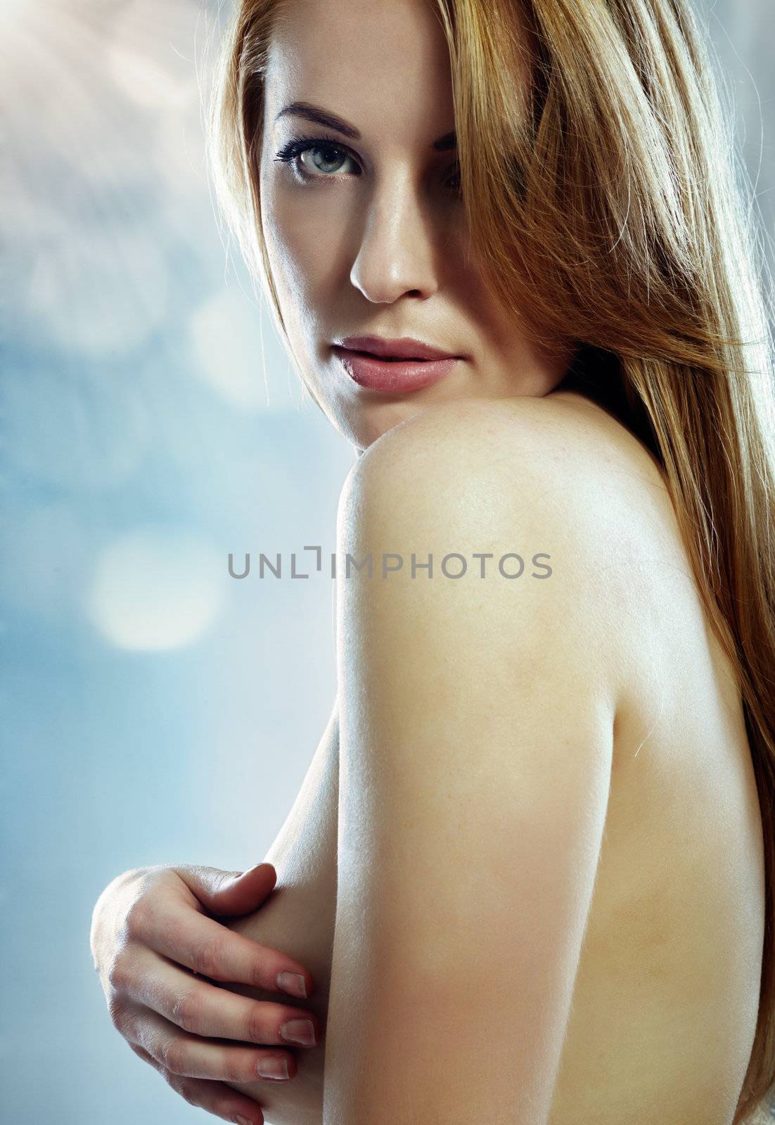 Sensual topless lady covering her breast by the hand on a blue background with bokeh