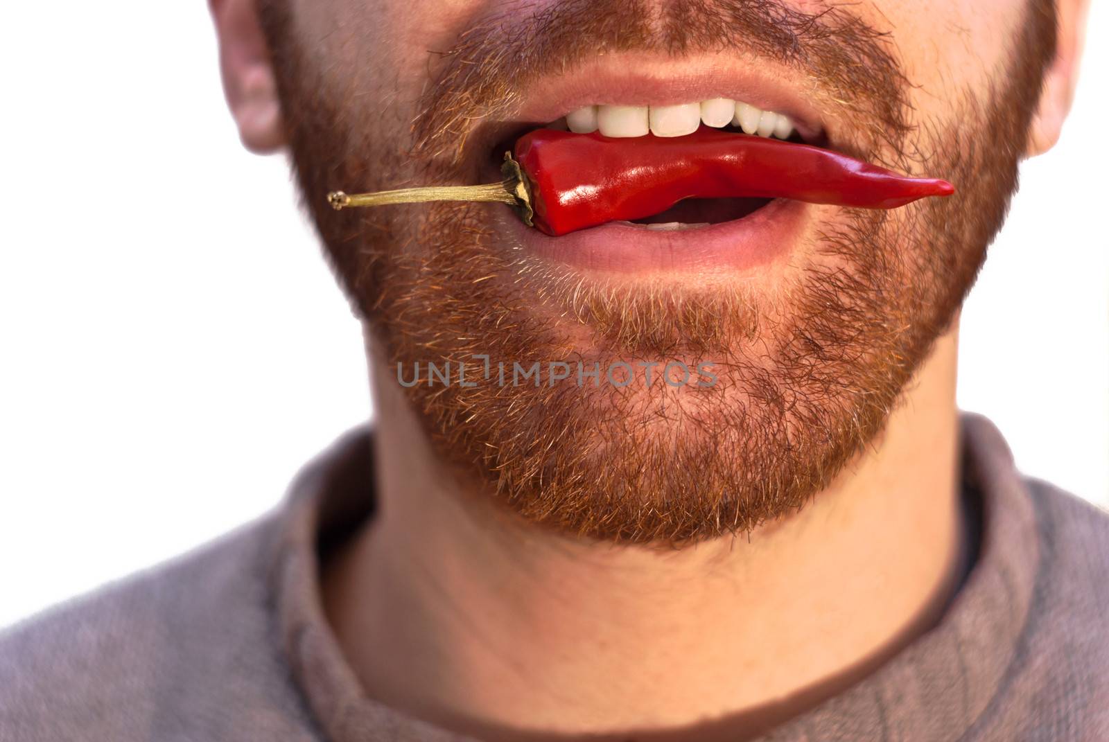 Young caucasian man with a red hot chili pepper in his mouth