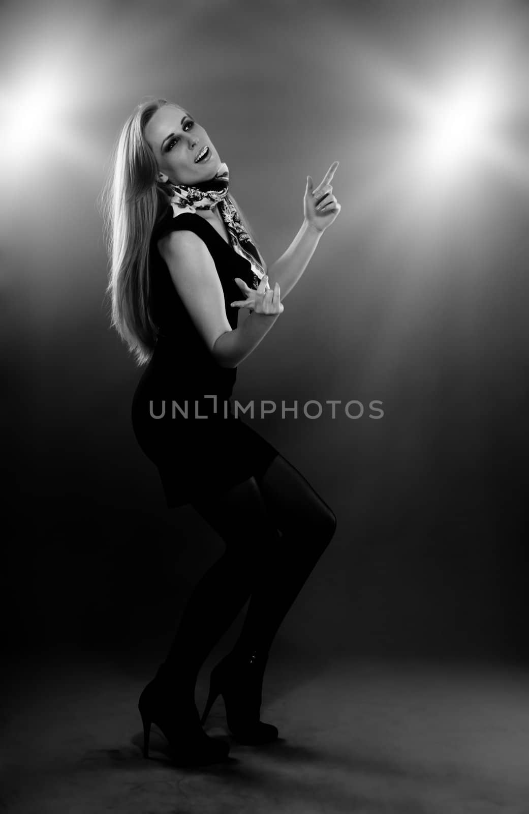 Smiling lady in the modern dress performing disco dance indoors with backlight and illumination. Black and white photo