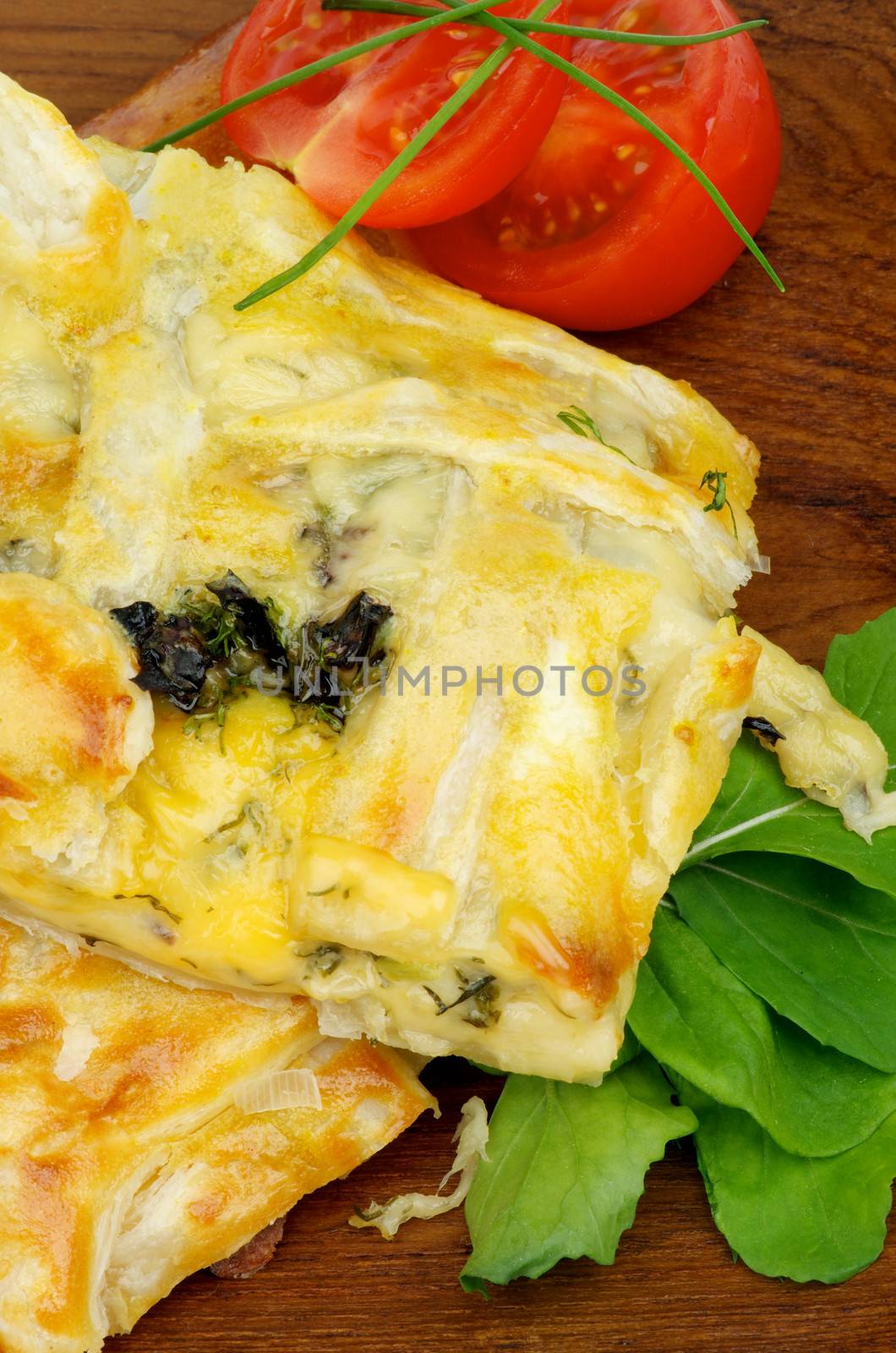 Slices of Cheese and Greens Pie Garnished with Tomatoes, Spring Onion and Basil on Wooden Plate closeup