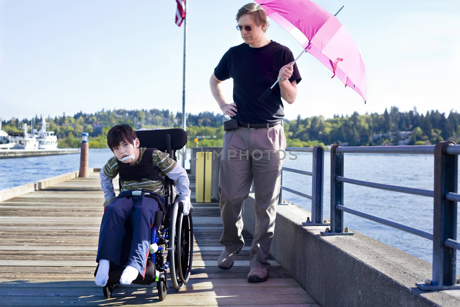 Father walking with disabled son out on lake pier by jarenwicklund