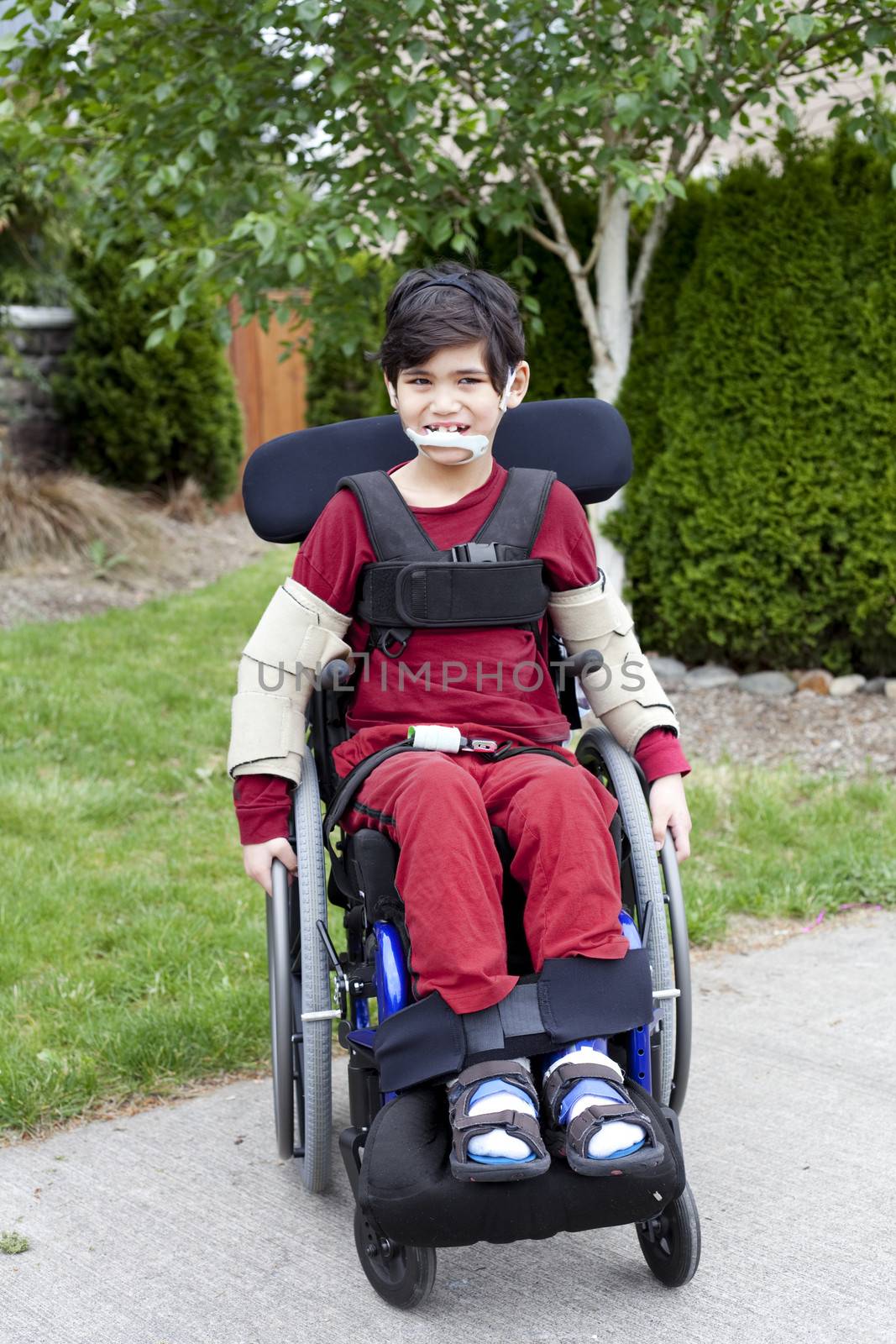 Disabled biracial six year old boy sitting in wheelchair on sidewalk