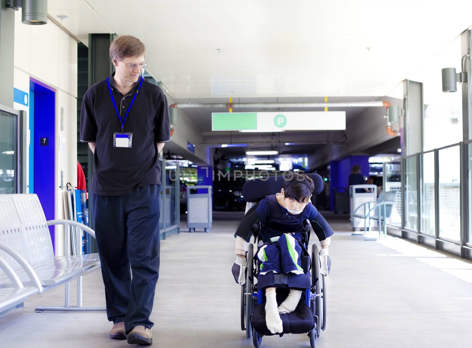 Father walking with disabled son in wheelchair to the hospital by jarenwicklund