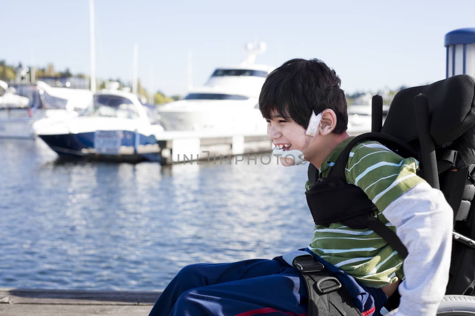 Disabled biracial six year old boy pushing himself in wheelchair on lake pier