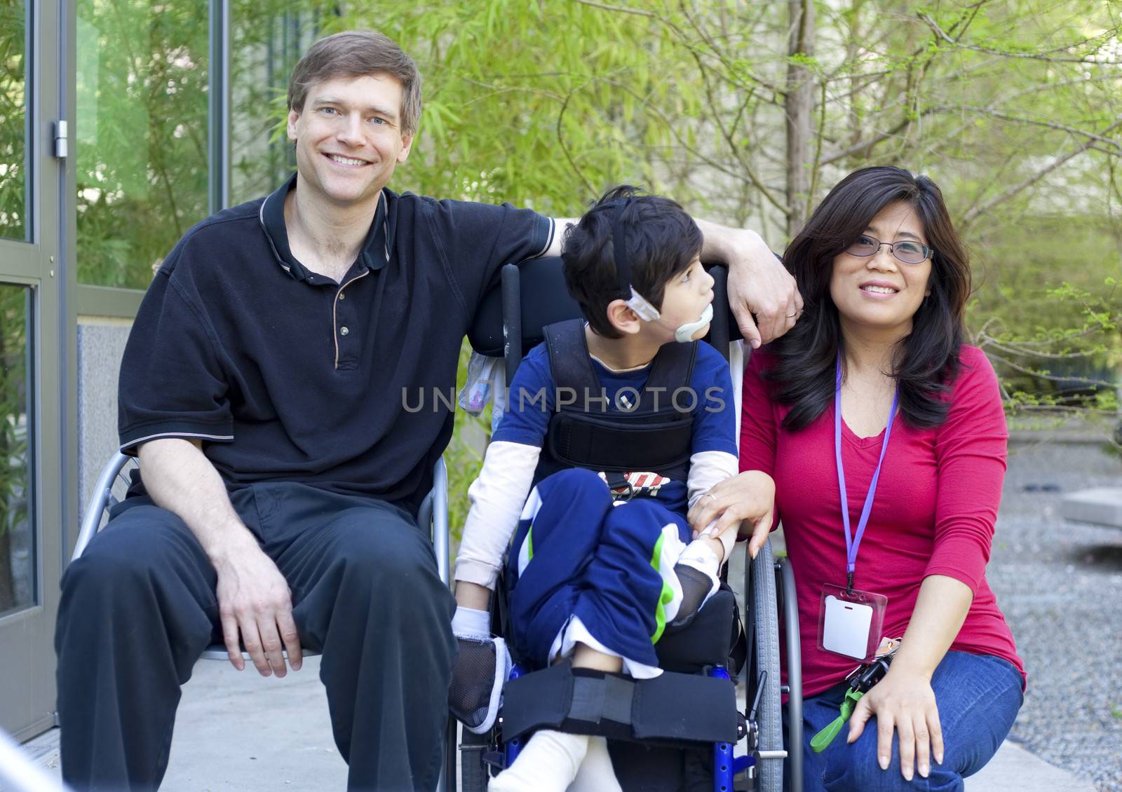 Disabled biracial six year old boy in wheelchair with parents outdoors