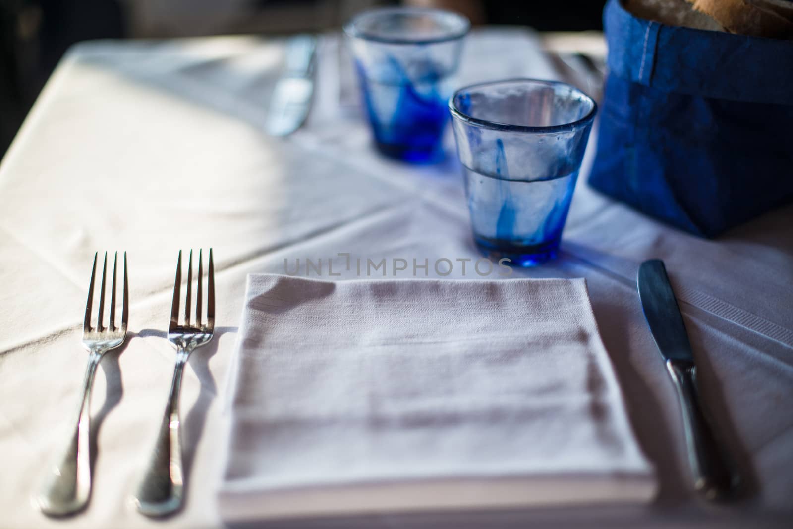 Table set for cozy dinner with blue glasses, bread basket and cutlery