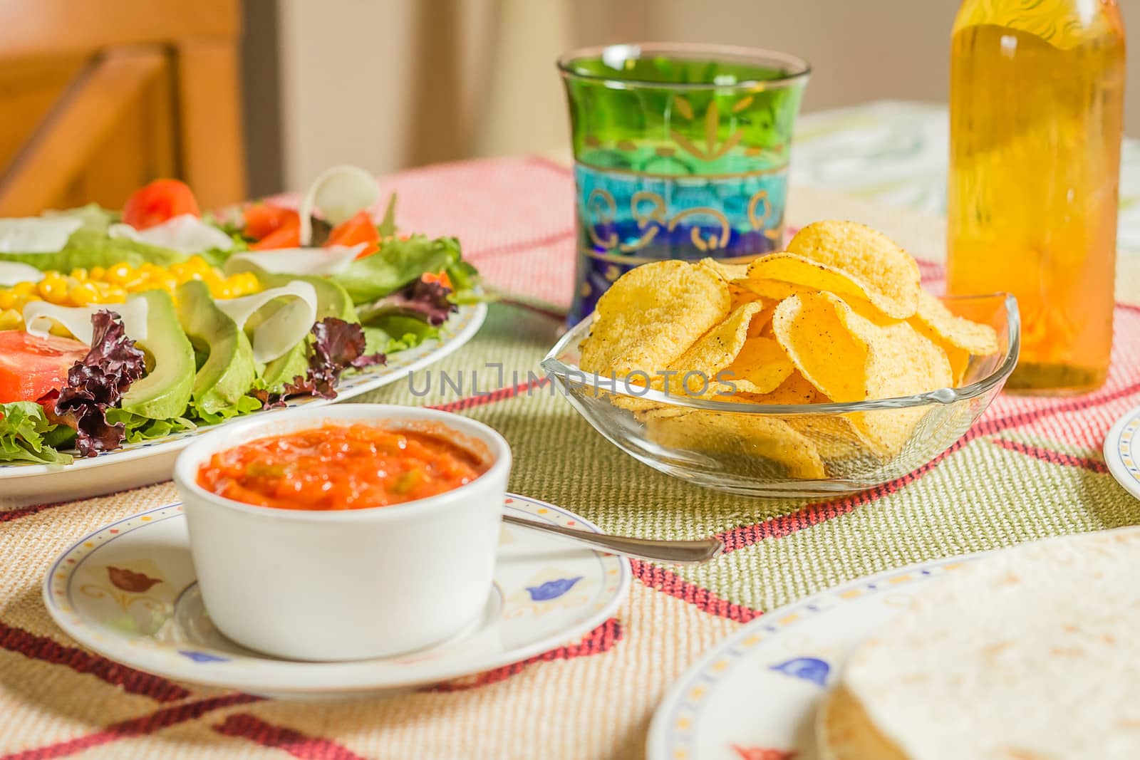Closeup of traditional mexican food in a table, with  a bowl of nachos, spicy sauce, a plate of tortillas and fresh salad