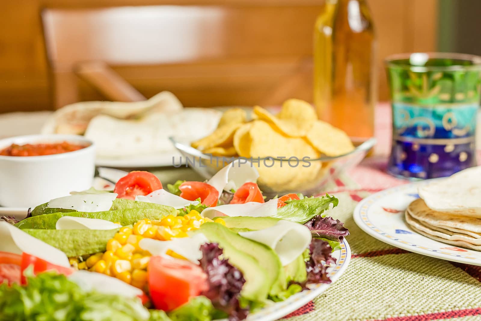 Closeup of traditional mexican food in a table, with a plate of fresh salad, tortillas, chicken fajitas, nachos and a bowl of spicy sauce