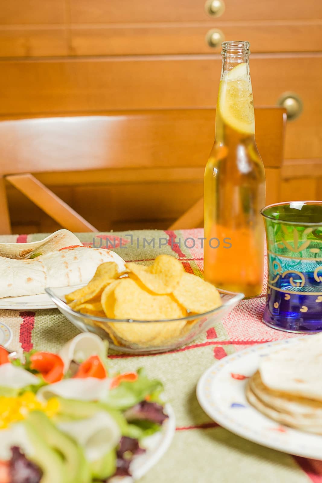 Closeup of traditional mexican food in a table, with  a bowl of nachos, a plate of chicken fajita, tortillas, fresh salad and a fresh beer