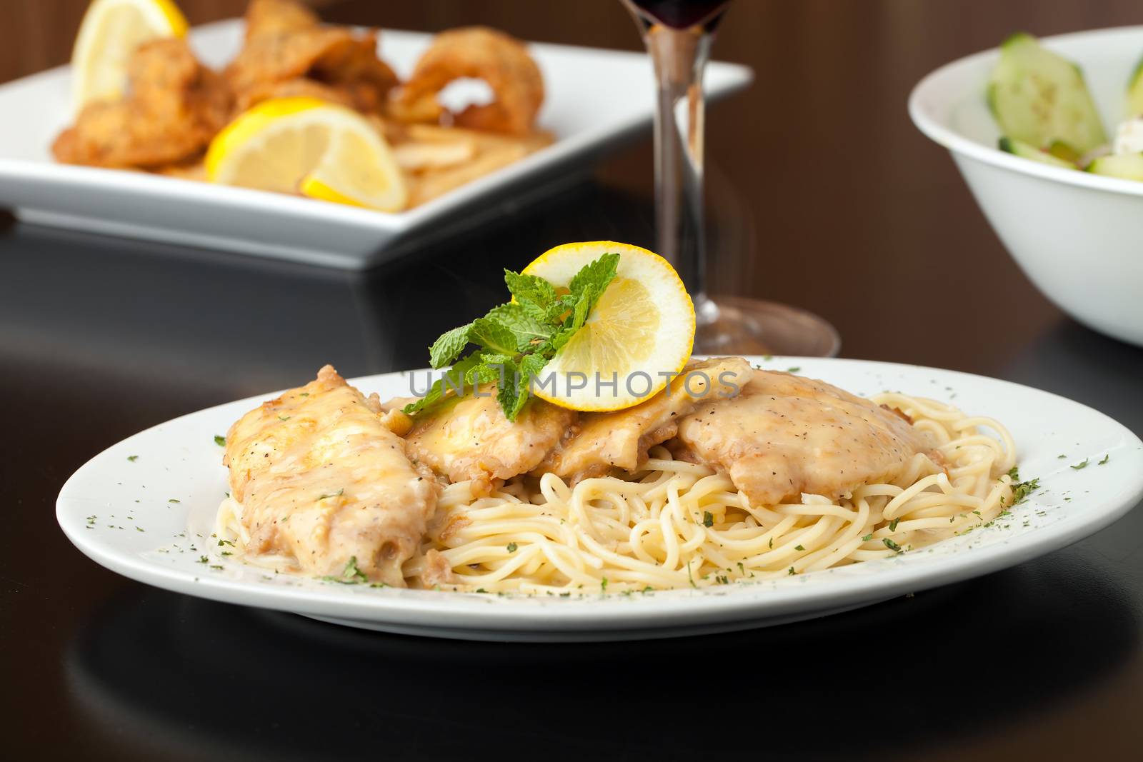 Chicken francaise or francese plated with pasta with salad and fried shrimp appetizer in the background.