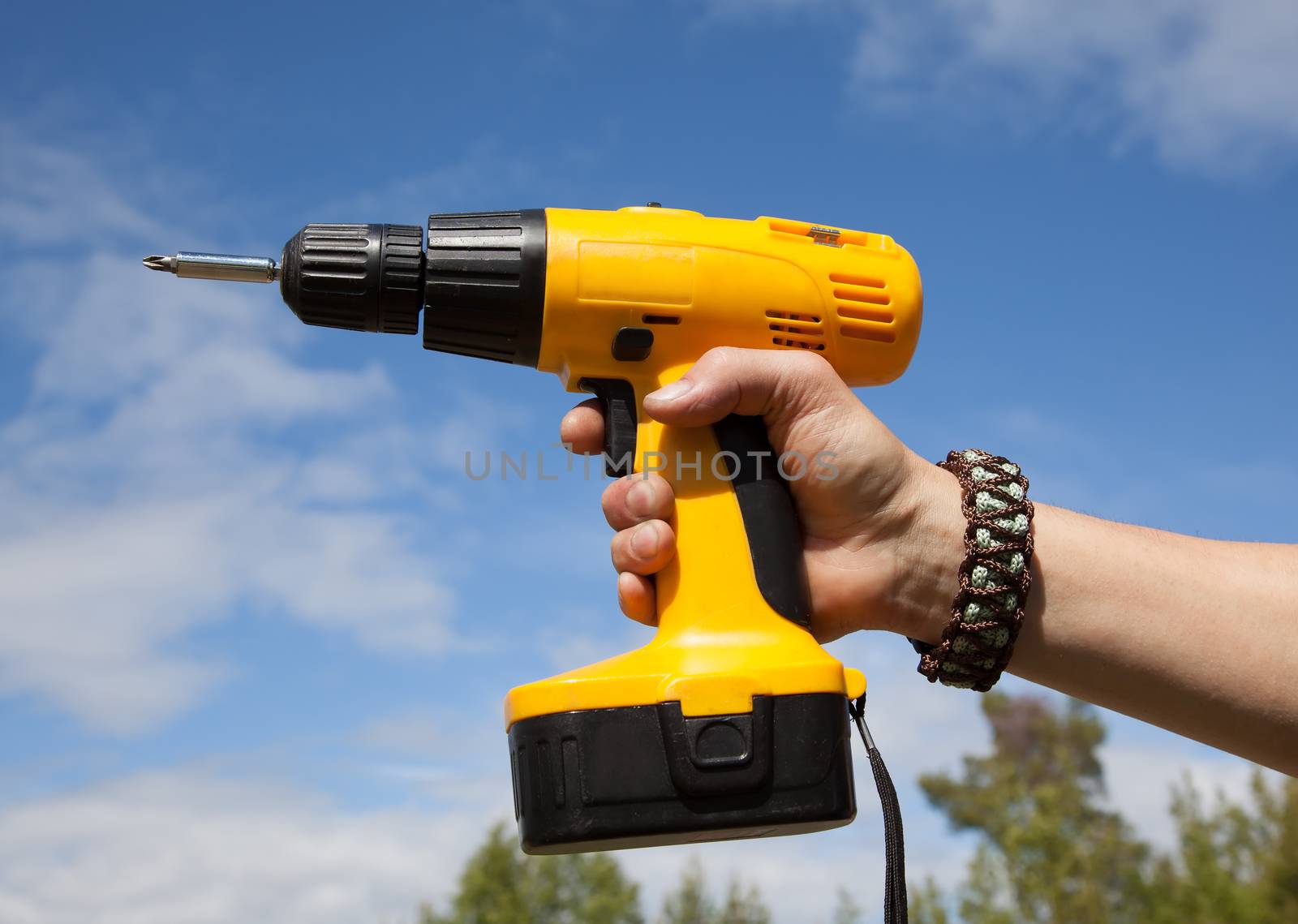 Man's hand in a yellow wristband holding screwdriver against the blue sky.