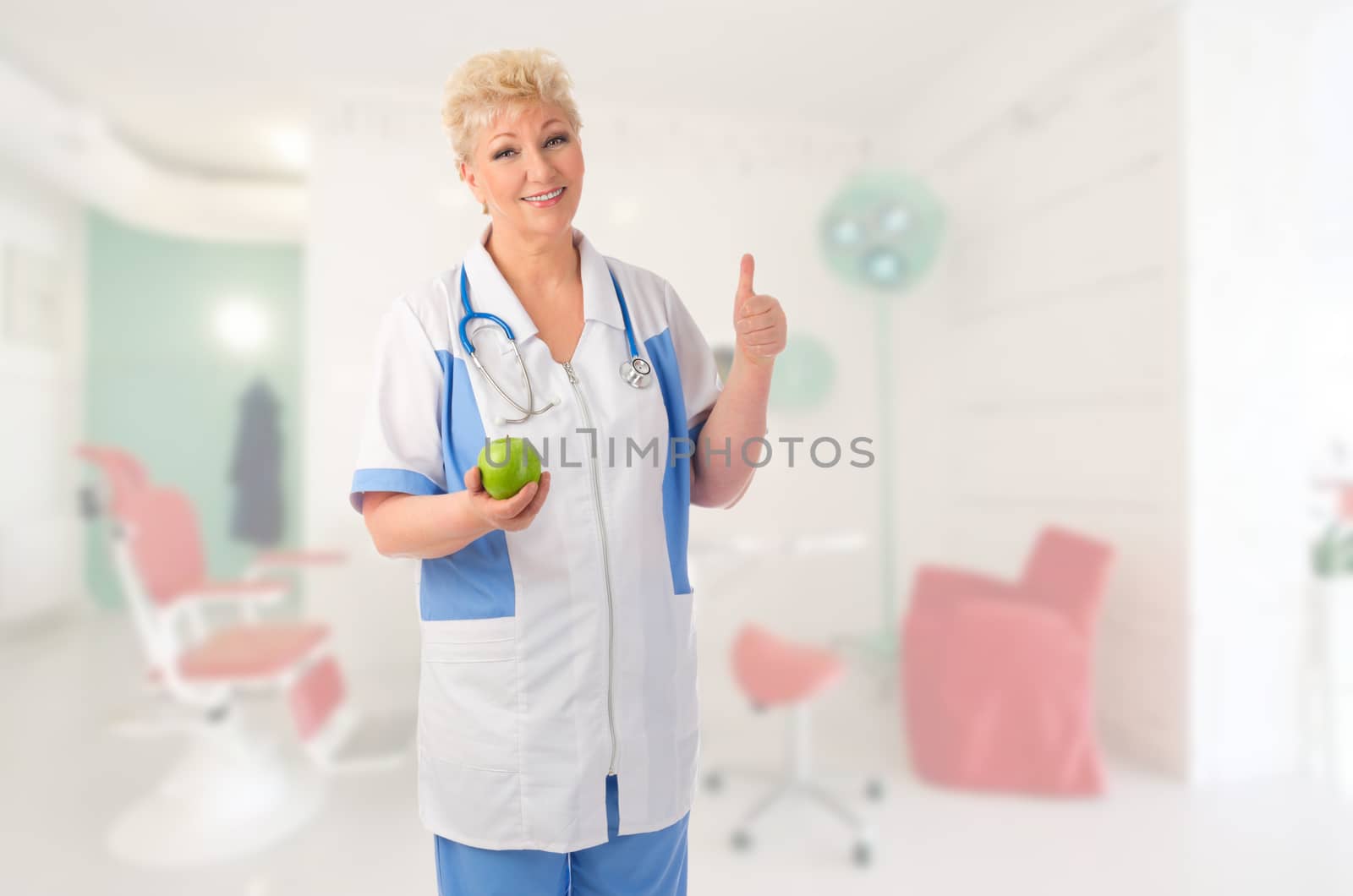 Mature doctor with green apple shows ok gesture at medical office